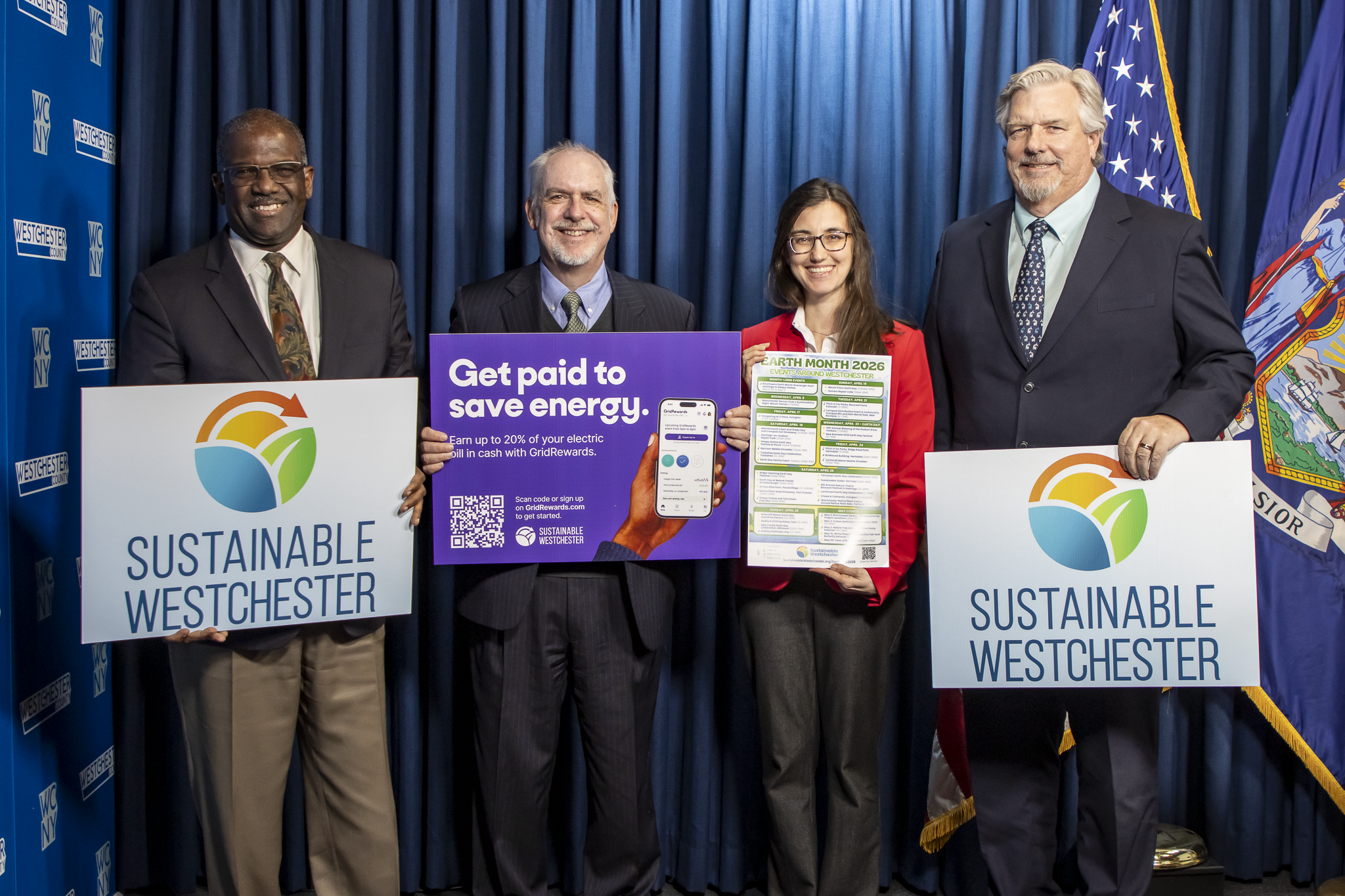 3 men and a woman posing for picture on stage holding Sustainable Westchester signage